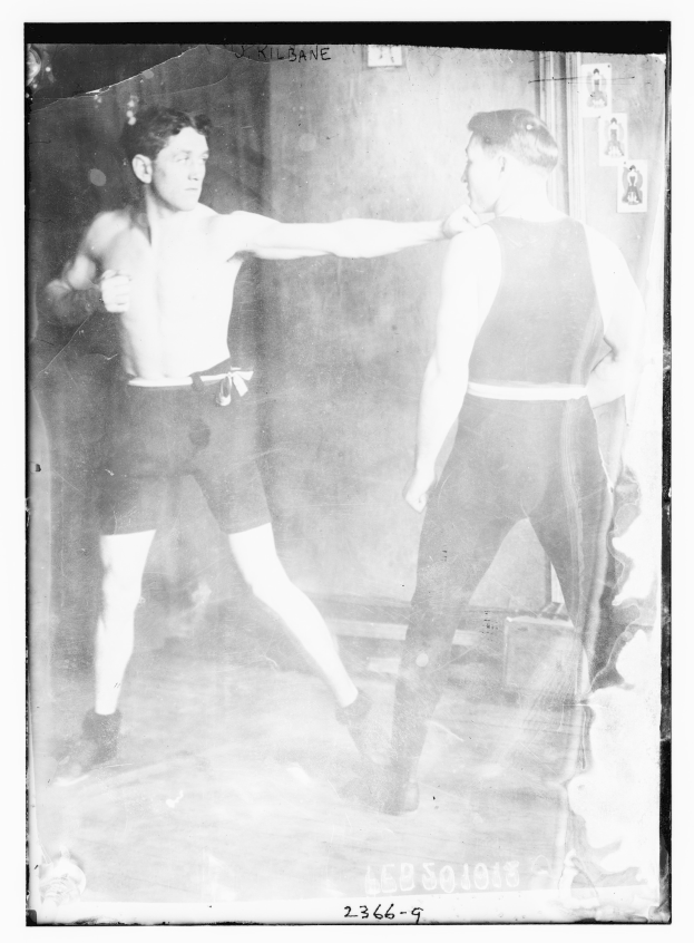 Schwarzes und wei├čes Foto von zwei Boxern in einem Boxring mit Postern an der Hintergrundwand und Text unten.