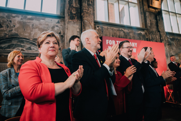 Eine Gruppe von Menschen, die vor einer Menge jubeln und eine Fahne im Hintergrund halten.