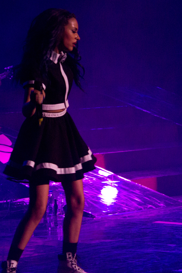 Eine Frau in einem schwarzen Kleid h├Ąlt ein Mikrofon, waehrend sie tanzt.