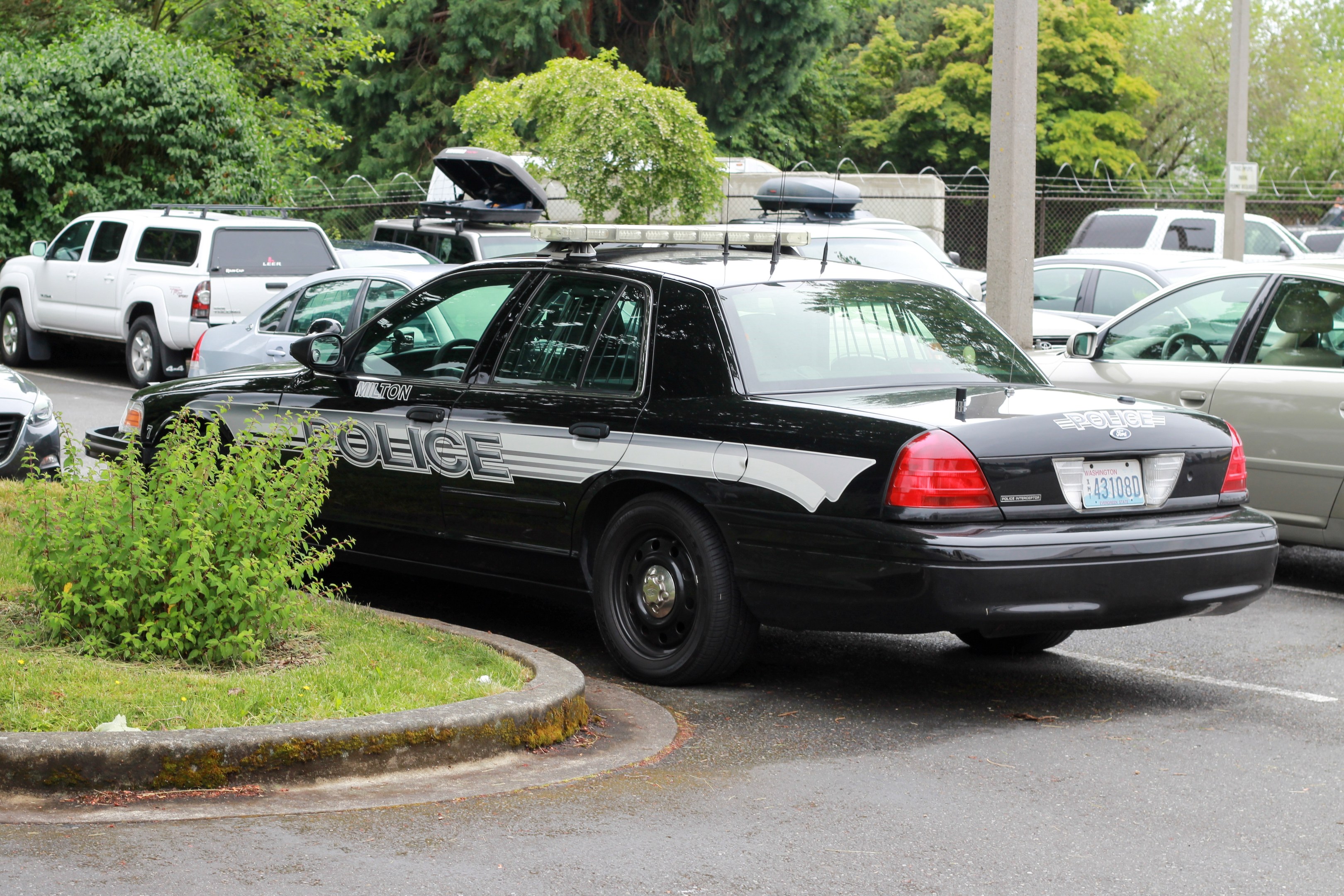 Polizeiauto auf einem Parkplatz mit Gras, Bäumen und Maschendrahtzaun