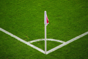 Ein Fußballfeld mit grünem Rasen, weißen Begrenzungslinien und einem weißen Pfosten mit einer roten und weißen Flagge auf dem zentralen Elfmeterpunkt.