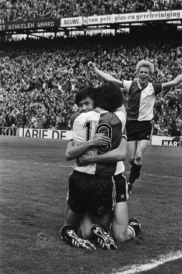 Drei Fussballspieler feiern ein Tor auf dem Boden in einem schwarz-weissen Stadion.