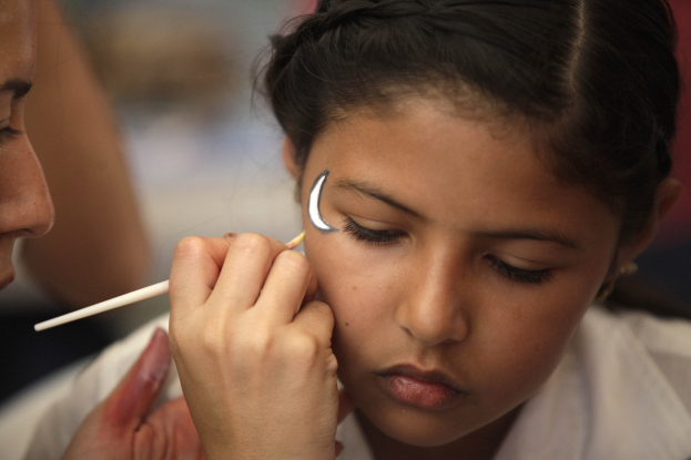 Ein junges Mädchen sitzt, während ein Make-up-Artist ihm Make-up mit einem Pinsel aufträgt, mit einem unscharfen Hintergrund.
