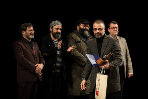 Eine Gruppe Männer steht auf einer Bühne bei Nacht, einer hält eine Tasche und eine Trophäe und feiert die Eröffnung des Berliner Filmfestivals.