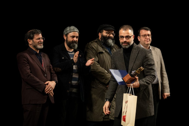 Eine Gruppe Männer steht auf einer Bühne bei Nacht, einer hält eine Tasche und eine Trophäe und feiert die Eröffnung des Berliner Filmfestivals.