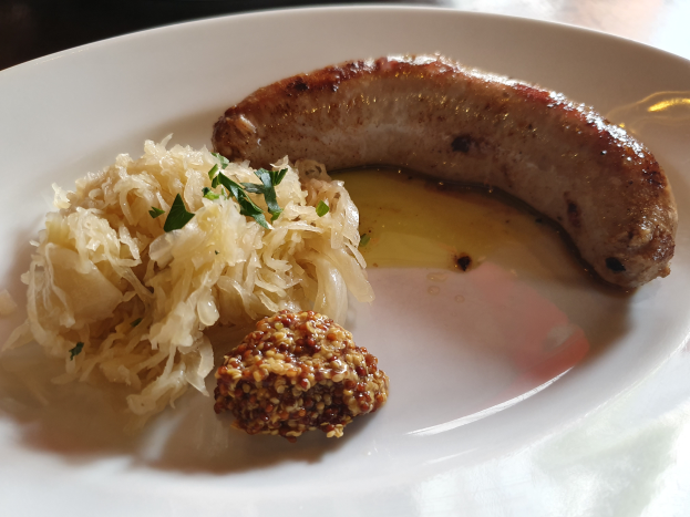 Ein weißer Teller, der mit Sauerkraut, deutscher Wurst und anderen Speisen bedeckt ist, gezeigt in einer Nahaufnahme auf einem Tisch.