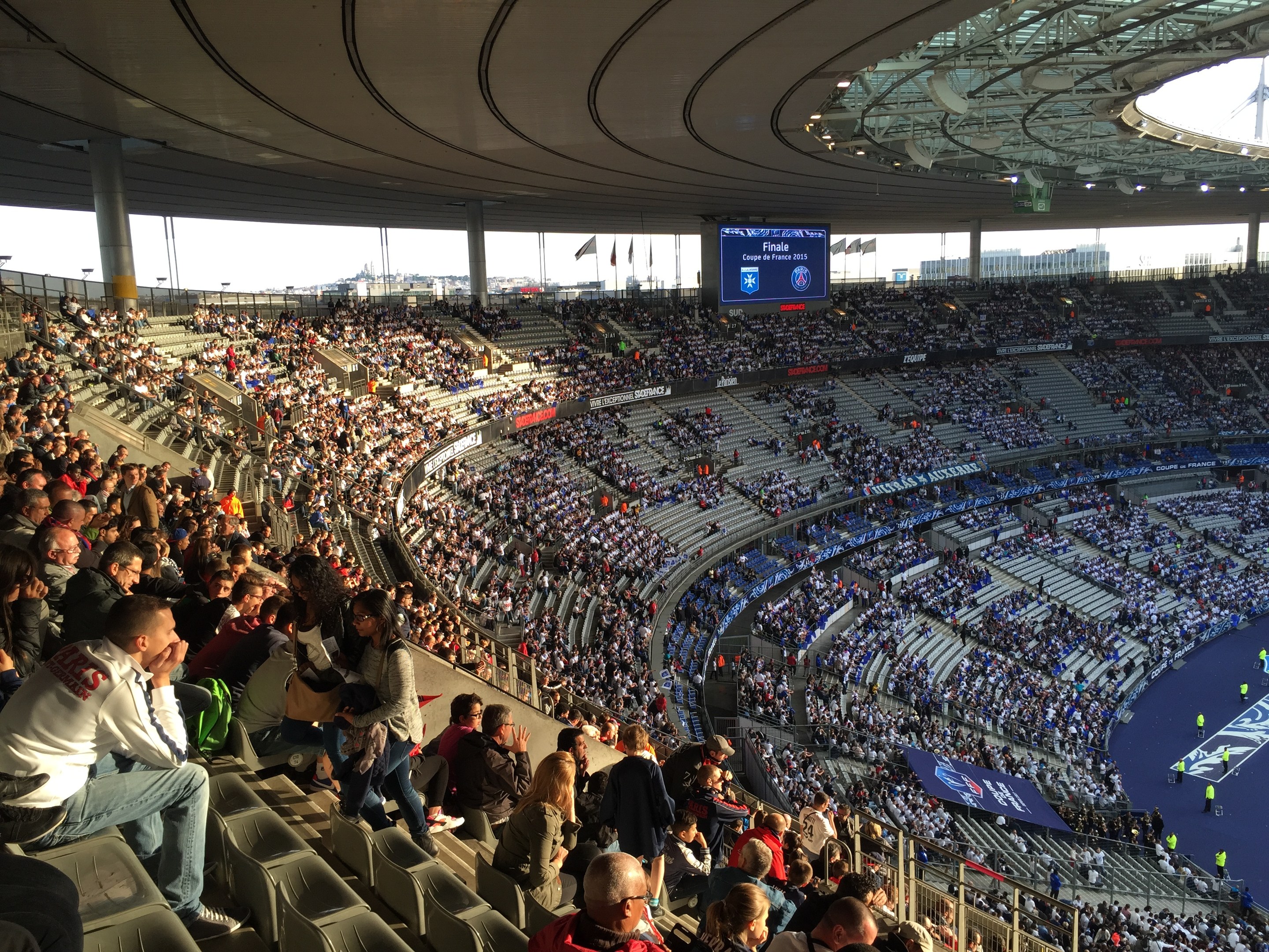 Große Menschenmenge in einem Stadion bei einem Fußballspiel mit einer Bühne, Flaggen und einem Bildschirm im Hintergrund auf der Allianz Arena in München, Deutschland.