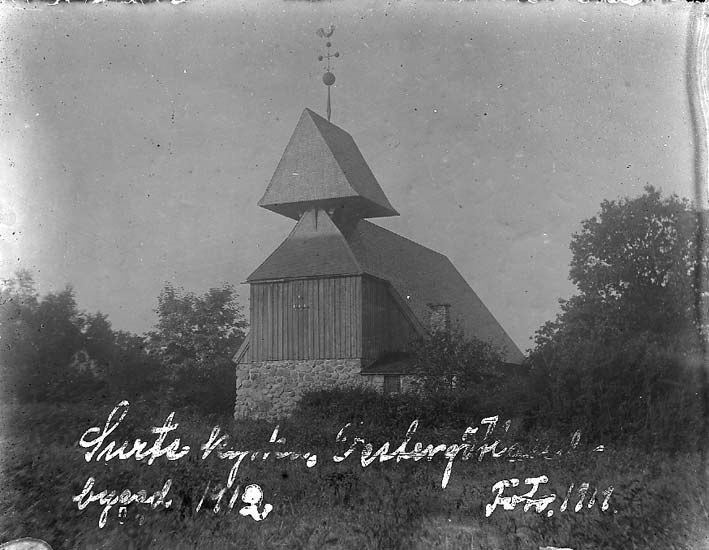 Schwarzes und weißes Foto einer Kirche mit einem Kirchturm, umgeben von Bäumen und Pflanzen, unter einem bewölkten Himmel, beschriftet mit "Kirche des Heiligen Grabes" unten.