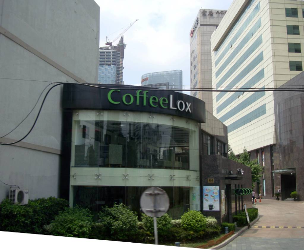 Ein kommerzielles Gebäude mit ein paar Pflanzen davor, umgeben von vielen hohen Gebäuden im Hintergrund, mit einigen Drähten sichtbar.