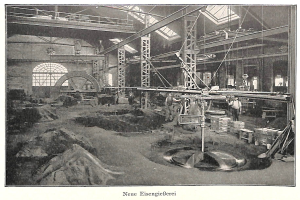 Ein altes Schwarz-Weiß-Foto einer Fabrik mit Arbeitern, die eine Maschine bedienen, umgeben von Metallstäben und Polen, mit dem Text "Neue Eisenglebeerei, die erste Fabrik in Deutschland" unten.