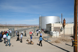 Eine spärliche Szene mit wenigen Menschen, einem Hund, Häusern, Zaunpfählen und einem Himmel.