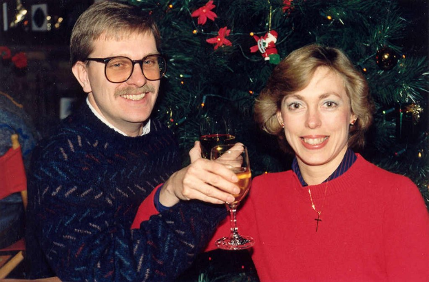 Ein Paar lächelt, whährend es Gläser Wein hält, mit einem Weihnachtsbaum im Hintergrund.