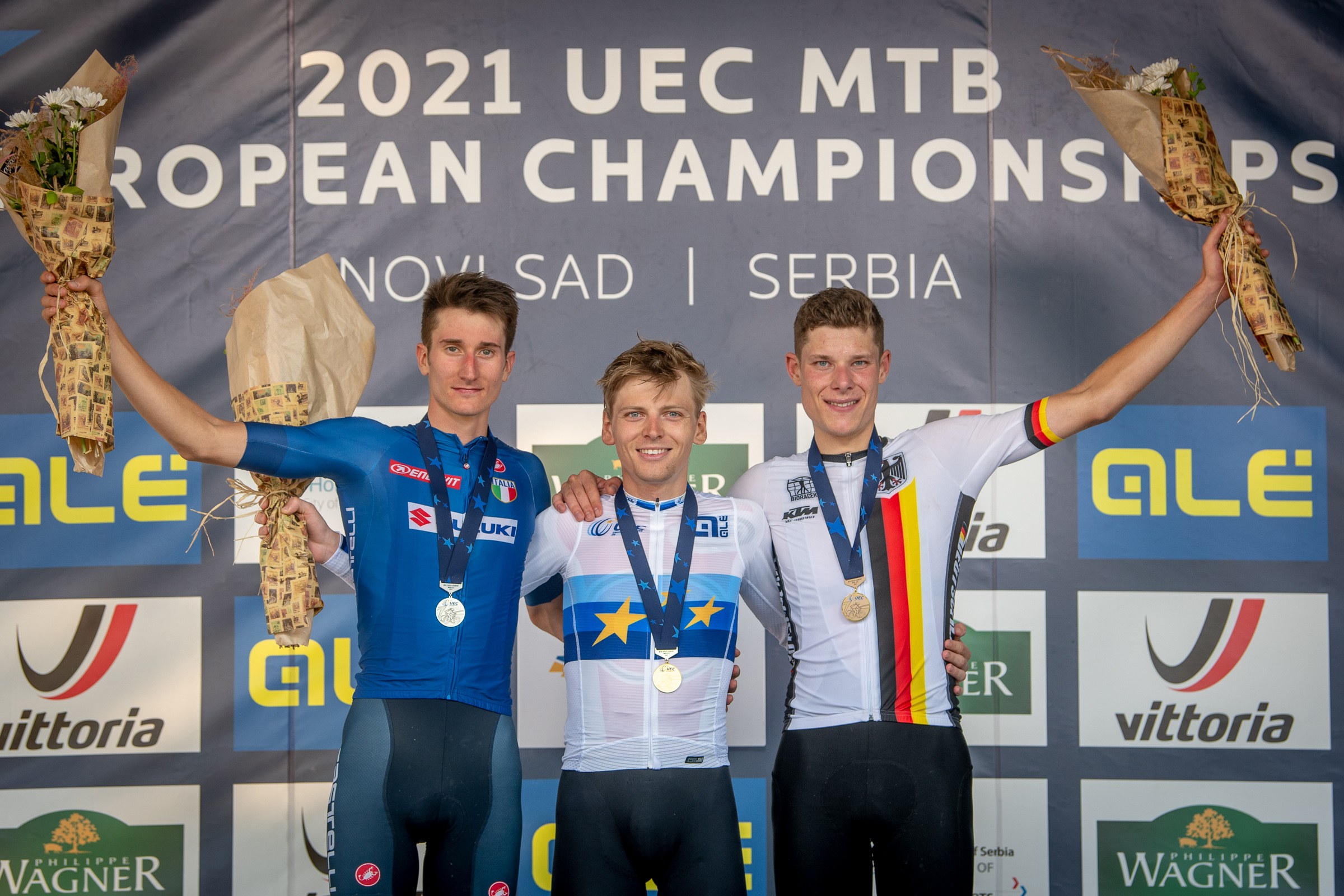 Drei medaillenreiche Männer auf dem Podium der UEC MTB Europameisterschaften 2021, jeder hält einen Blumenstrauß in der Hand.