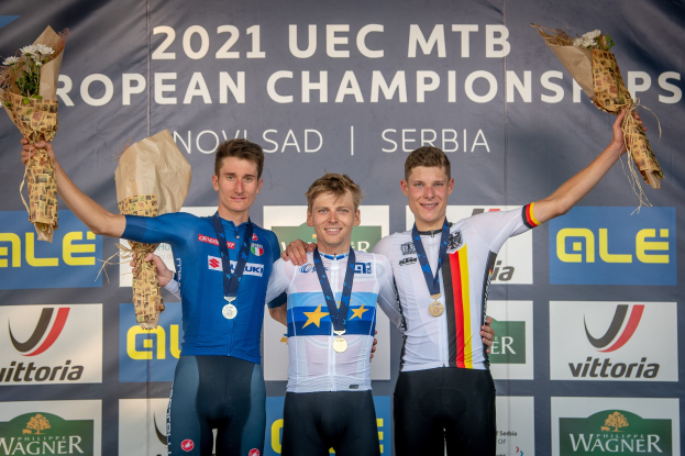 Drei medaillenreiche Männer auf dem Podium der UEC MTB Europameisterschaften 2021, jeder hält einen Blumenstrauß in der Hand.
