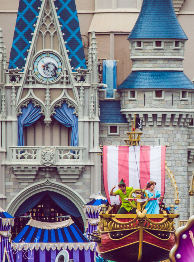 Eine bootähnliche Struktur mit tanzenden Menschen darauf, eine Fahne und ein Gebäude mit einer Uhr und Vorhängen im Hintergrund.