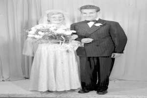 Ein Mann und eine Frau stehen nebeneinander auf einer Bühne, lächeln und die Frau hält einen Blumenstrauß in der Hand.