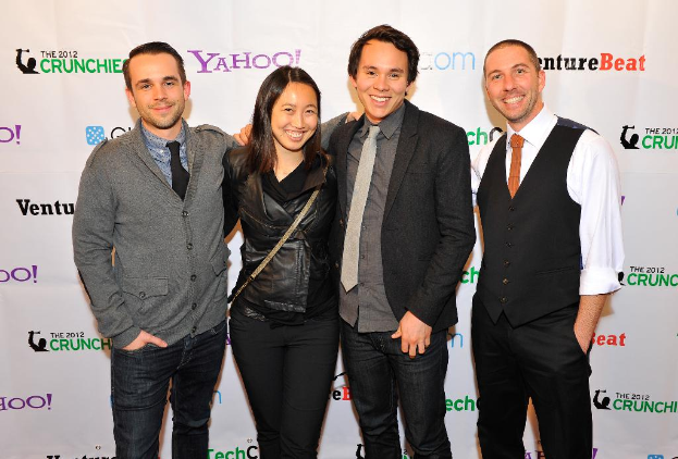 Eine Gruppe strahlender Menschen, die für die Kamera posieren, mit einem Sponsorenbanner im Hintergrund.