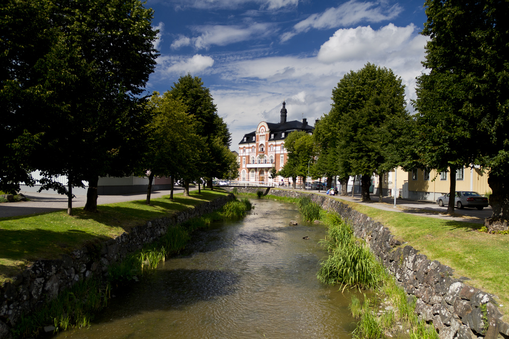 Ein von Bäumen und Straßen gesäumter Kanal mit Autos auf der Straße und einem Haus im Hintergrund unter einem blauen Himmel.
