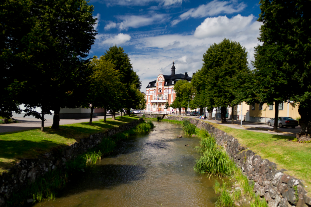 Ein von Bäumen und Straßen gesäumter Kanal mit Autos auf der Straße und einem Haus im Hintergrund unter einem blauen Himmel.