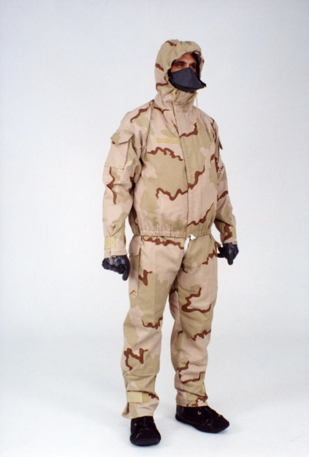 Eine Person in einem camouflagegemusterten Schutzoverall und einer Maske steht vor einem weißen Hintergrund.