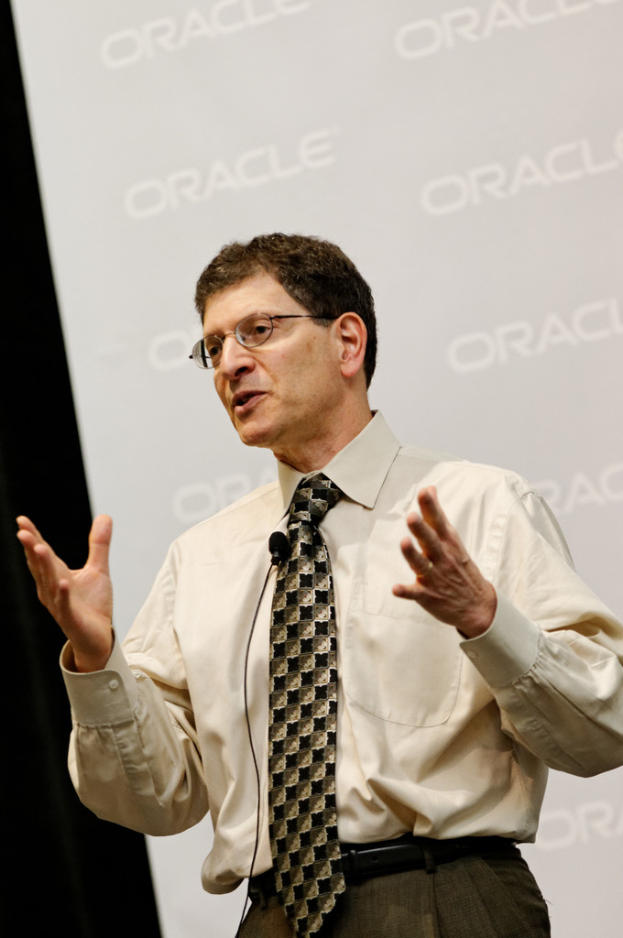 Eine Person steht vor einer Sponsorentafel und trägt Kleidung und eine Brille.