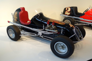 Zwei Oldtimer-Rennwagen in einem Museum ausgestellt, auf dem Boden stehend mit einer Wand im Hintergrund.