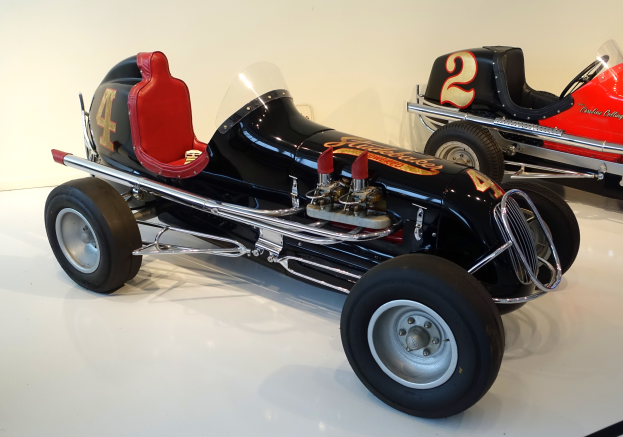 Zwei Oldtimer-Rennwagen in einem Museum ausgestellt, auf dem Boden stehend mit einer Wand im Hintergrund.